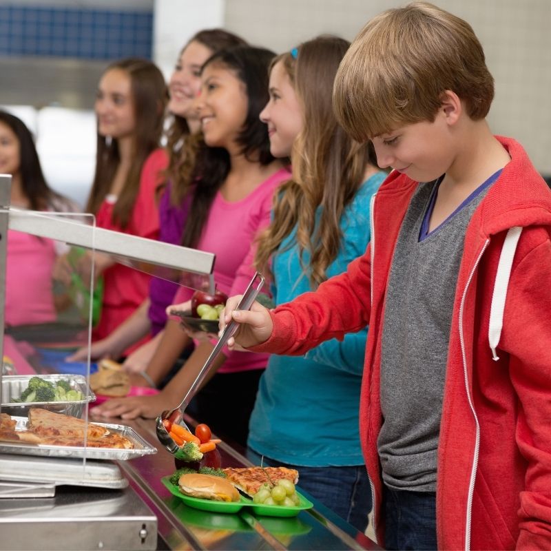 Kinder stehen an der Essensausgabe einer Kantine und befüllen ihre teller